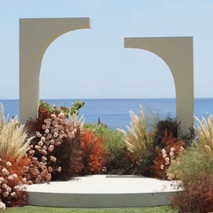 A white asymmetrical modern archway and platform surrounded by flowers